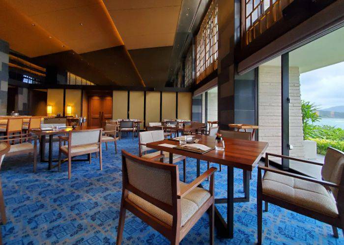 The high ceilings, modern stylings and blue carpet of Aomi (Halekulani Okinawa Hotel), with windows overlooking the ocean.